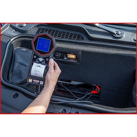 Eine Person hält ein rotes und schwarzes Diagnosegerät. Das Gerät ist mit einem Auto verbunden, das Ergebnis wird auf einem Bildschirm angezeigt.